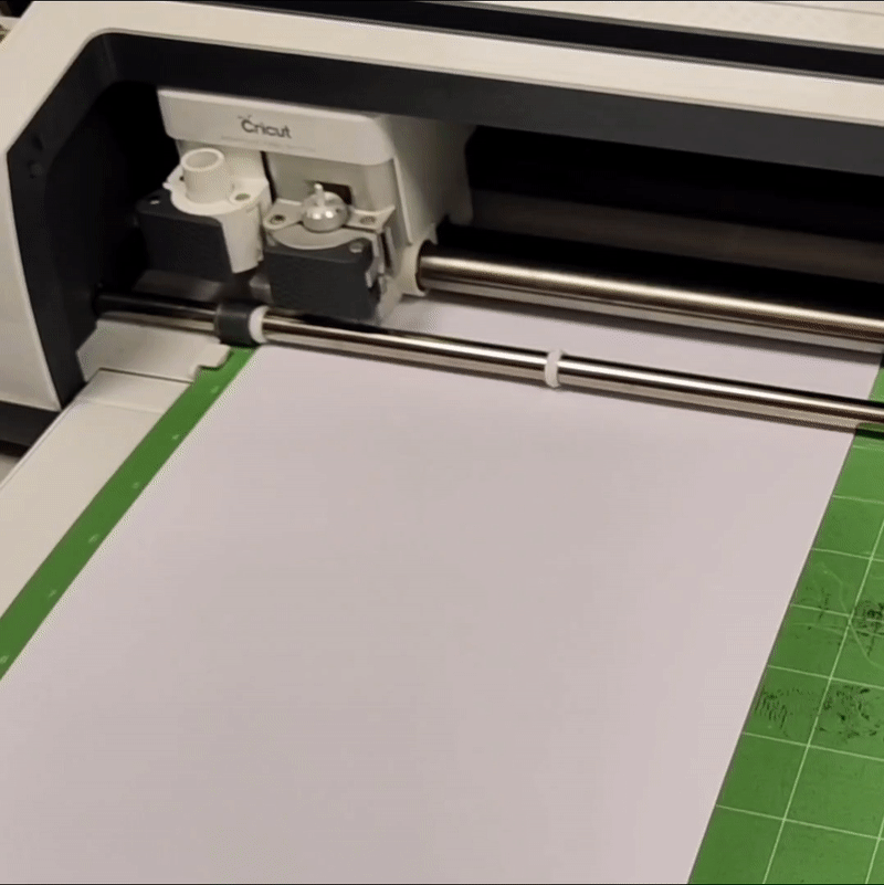 animated photo showing the Cricut machine cutting a design. It has a small knife attached to it, and it moves up and down around the paper cutting the outline.